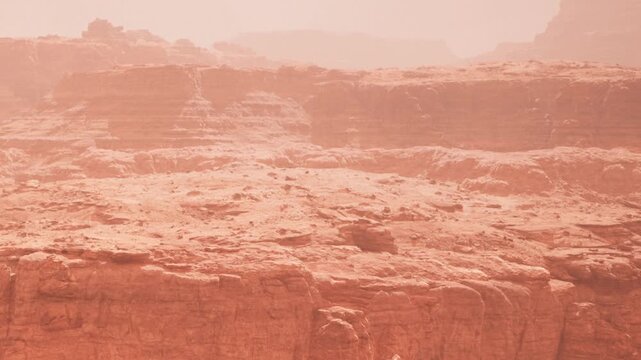 Rock formations and dusty ground stretch across a vast desert area. The sky is unclear with a hazy look. This scene shows barren land with no signs of life during the day.