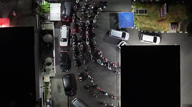 Aerial view of SPBU 54.803.22 DALUNG Pertamina gas station at night with a long queue of motorcycles and cars waiting to refuel in Kecamatan Kuta Utara, Bali, Indonesia.