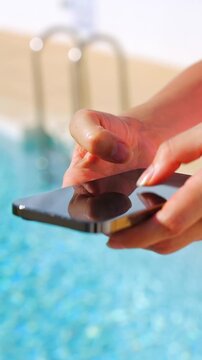 Close-up of female hands typing on a smartphone by a pool
