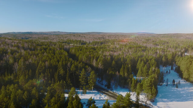 An expansive aerial view reveals a snow-covered conifer wilderness and winding frozen waterway beneath soft winter light, showcasing the quiet, remote terrain of the Ural Mountains in Russia