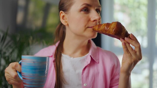 Woman enjoying a fresh croissant and coffee for breakfast.