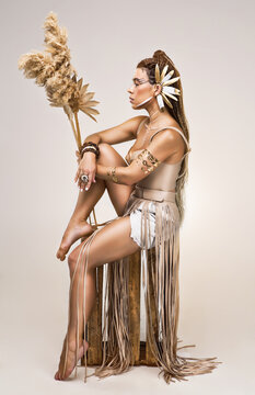 Premium conceptual fine art portrait of young woman with tribal makeup, gold feathers ear cuff and pampas grass