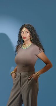 Vertical video: Indian woman posing in studio, turning to frontal, adjusting green-gold jewelry