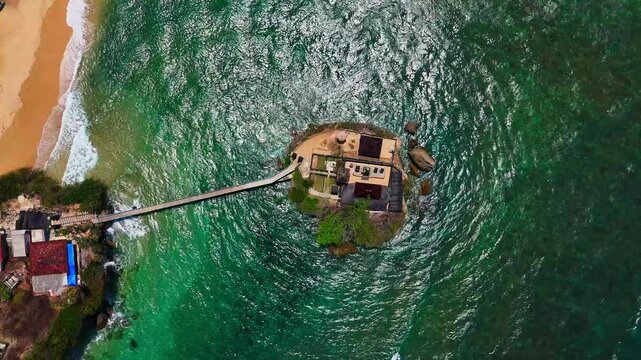 Aerial view of Balekambang Beach with its iconic temple on a small island connected by a bridge to the sandy coastline in Malang, East Java, Indonesia.