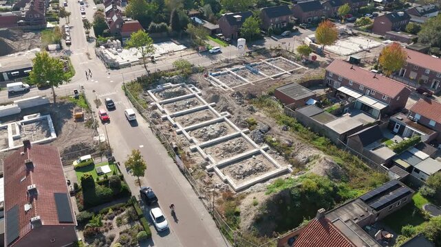 Aerial drone shot of a newly laid concrete foundation for a new-build house in the middle of a residential neighborhood, surrounded by existing homes and streets.