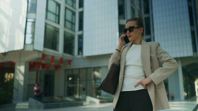 A confident business woman talks animatedly on her smartphone in a modern urban setting. She is engaged in a serious conversation while standing in front of an office building.