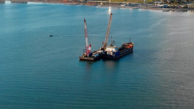 Floating work platform and dredging vessel during coastal maintenance. Marine infrastructure scene with sediment removal equipment