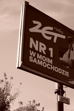 Large Radio ZET billboard rises above a Poznań street beneath a warm sepia-toned sky