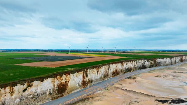 Wind farm and solar panel field stretch along farmland above Normandy coastline. Clean energy infrastructure near English Channel and chalk cliffs