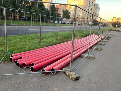 Red plastic pipes stacked behind temporary metal construction fence