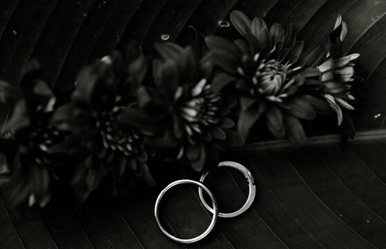 Black and white macro shot of wedding rings placed on a textured leaf with flowers