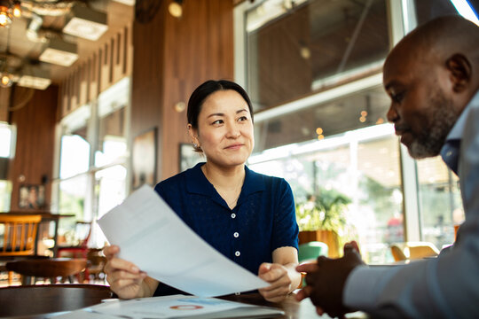 Smiling woman reviewing documents with colleague in cafe