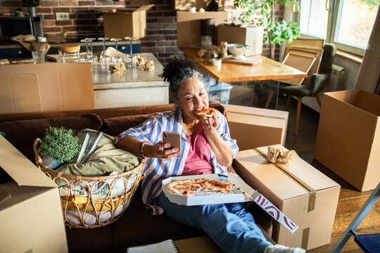 Senior woman eating pizza and checking phone during move