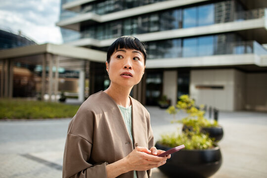 Woman looking around while checking smartphone outside apartment building