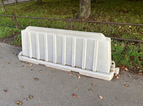 Single white plastic traffic barrier on sidewalk near metal fence