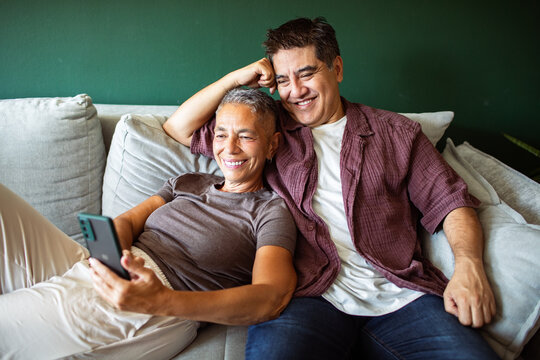 Smiling couple relaxing on sofa looking at smartphone