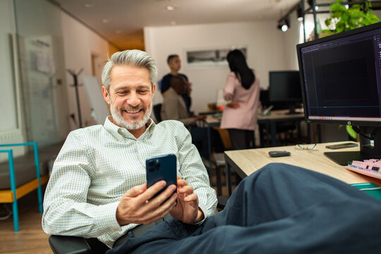 Smiling middle-aged man checking smartphone in open office