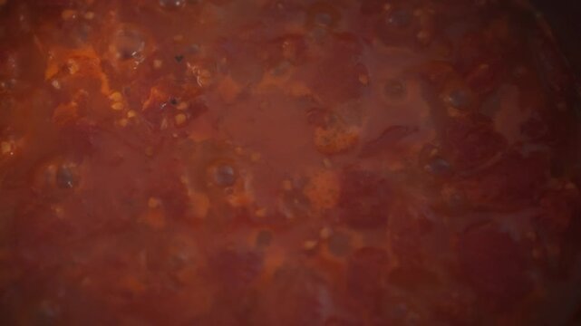 Top view of tomato sauce actively boiling in a metal pot. Tomato pulp pieces and bubbles fill the surface. Theme of homemade sauce preparation and traditional cooking process