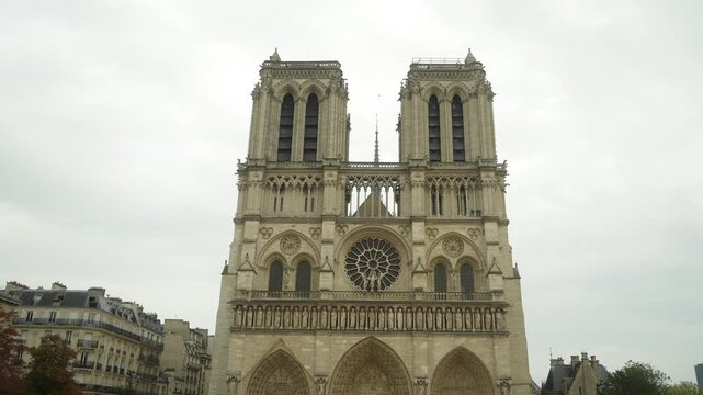 Front facade of Notre-Dame de Paris seen from ground-level perspective, twin bell towers framing central rose window and ornate stone portals, overcast sky creating soft diffused light over weather