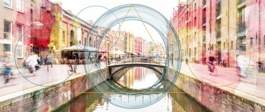 Cyclists passing canal bridge between brick warehouses framed by glass ring and gold triangle