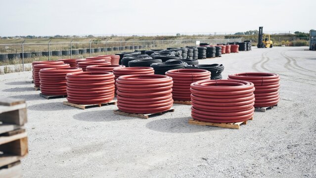 Industrial polyethylene pipe coils with orange and black colors stored outdoors for large scale utility infrastructure work.