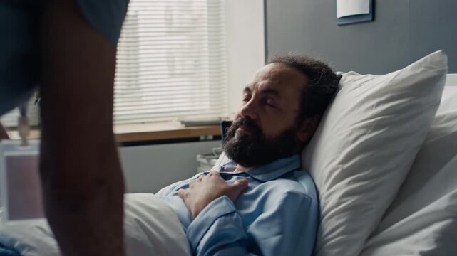 Middle aged Caucasian male patient lying in hospital bed while nurse tucks blanket, breathing heavily and resting. Footage suitable for healthcare campaigns and medical treatment commercials