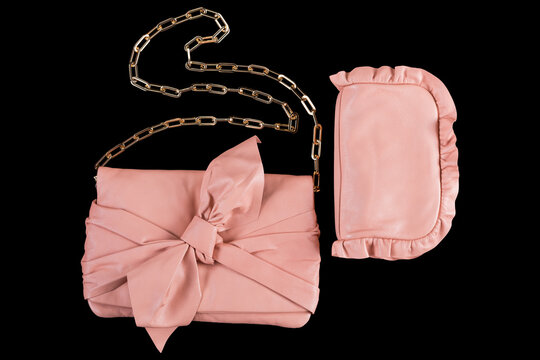 Pink leather womens clutch bag with bow and chain strap isolated on black background