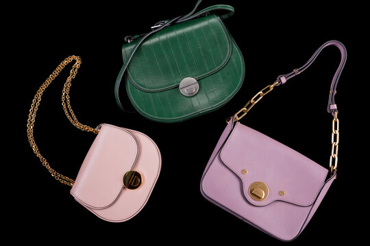 Three womens leather handbags set in green pink and lilac isolated on black background