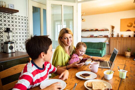 Mother multitasking on phone and laptop during family breakfast