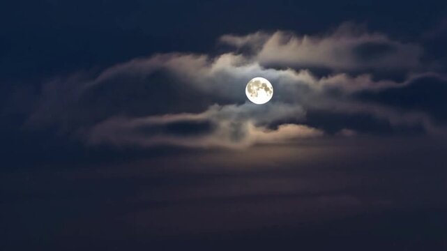 The full moon shone through the gaps in the dark clouds, casting a soft glow in the night sky.