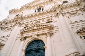 Close-up view of ornate classical church facade with tall fluted columns, decorative capitals, sculpted friezes and arched dark wooden entrance, photographed from low angle under soft daylight, warm-t © Dima Anikin