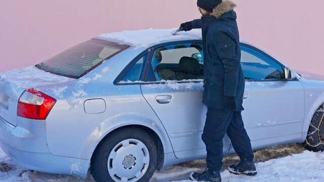 Albania, Boge 2026 01 11: A man scraping snow off the roof of a car in winter, medium shot, horizontal orientation.