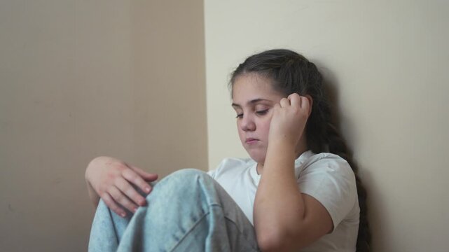 Young girl sitting on the floor. Sad child sits on a corner and is punished. A teenage girl is traumatized by a violent lifestyle incident. A little girl sitting on the ground.