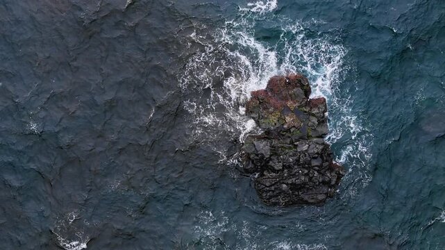 Powerful Atlantic water around isolated volcanic rock with white foam ring, aerial top down. Strong ocean texture and dark lava stone work well for energy, rough sea and natural background