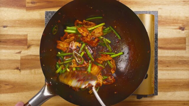 Stir-frying Twice Cooked Pork with fresh garlic sprouts and spicy broad bean paste in a hot wok. Real-time Asian cooking showcasing authentic Sichuan cuisine.