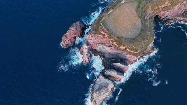 Sea stacks extend from rocky headland on Sao Miguel, Azores, Portugal. Top down footage of Atlantic Ocean surf around coastal cliffs with farmland above rugged shoreline