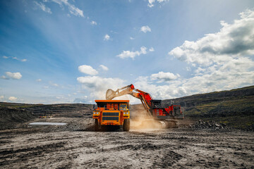 Concept mining industry, Industrial excavator loads coal into back of yellow heavy dump truck in open pit mine under bright sky © Parilov