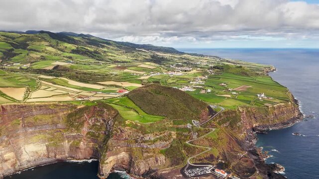 Green coastal countryside on Sao Miguel, Azores, Portugal, with farmland above Atlantic cliffs. Drone footage of patchwork agricultural fields across rolling island hills