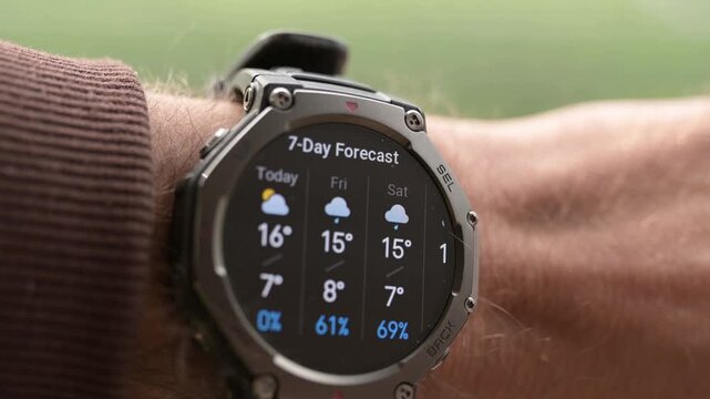 Close-up of rugged smartwatch on wrist showing weather forecast and temperature