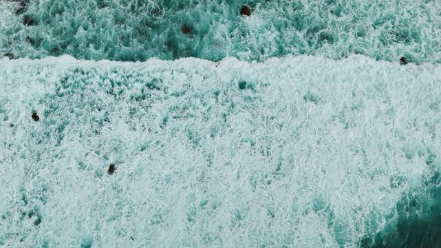 Powerful Atlantic wave breaking across ocean surface with dense white sea foam, top down aerial view. Natural ocean background with rough water texture