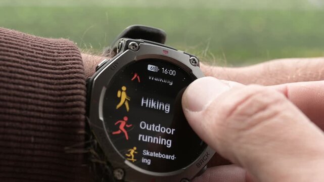 Close-up of hand scrolling rugged smartwatch menu to select outdoor running workout