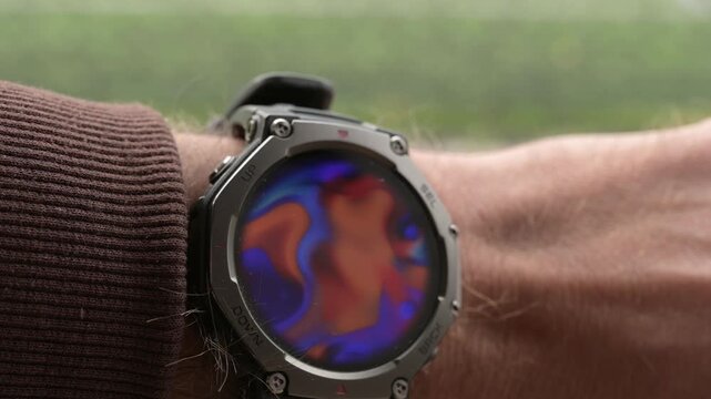 Close-up of rugged smartwatch on wrist showing colorful abstract fluid animation