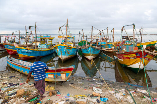 Fisherman walking toward colorful fishing boats on a littered shore, Northern Province, Jaffna, Sri Lanka