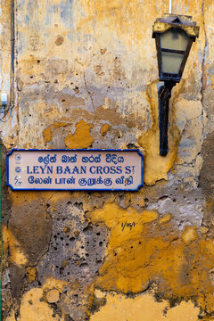 Trilingual street sign and old lamp on a weathered yellow wall, Southern Province, Galle, Sri Lanka