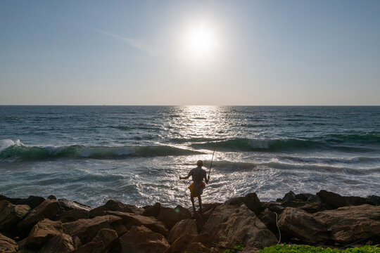 Silhouette of a fisher with a rod standing on rocks facing the sea, Western Province, Colombo, Sri Lanka