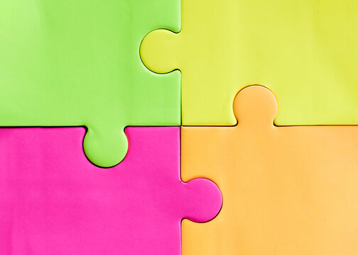 Four large colorful jigsaw puzzle pieces in green, yellow, pink and orange interlocking together. Bright abstract background for business teamwork, problem solving and education industry design.