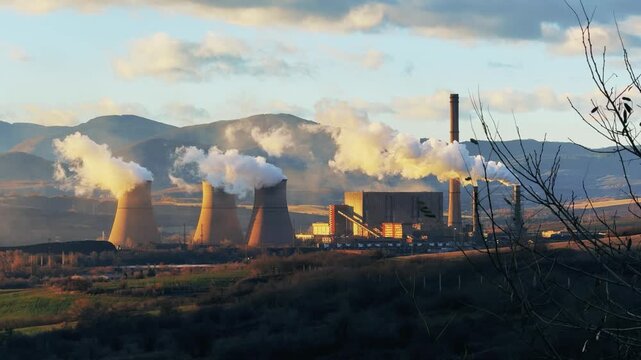 Thermal power plant with smoke plumes in a picturesque landscape at sunset
