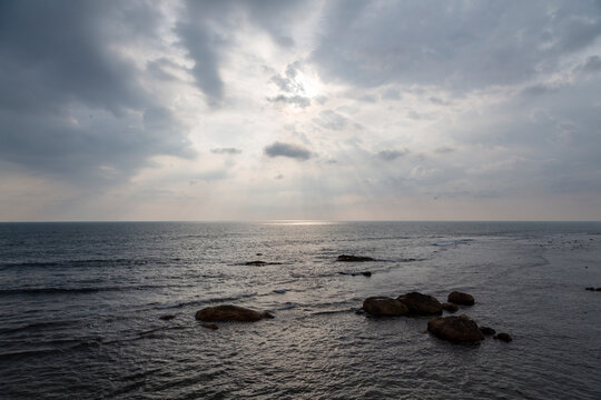 Sun rays through dark clouds over a calm sea with rocks, Southern Province, Galle, Sri Lanka