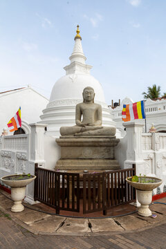 Seated Buddha statue in front of a white stupa with flags, Southern Province, Galle, Sri Lanka
