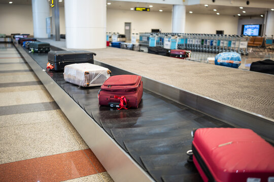 Many personal luggage transporting from airplane to arrival area in airport terminal, suitcases and bags lying on conveyor belt line, arrival zone with automatic carousel for passengers baggage. 
